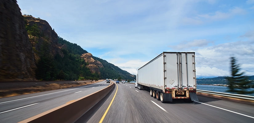 truckingstatisticsandfactsforfleetmanagers A truck drives on a highway, framed by towering mountains in the distance